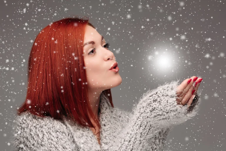 beautiful young girl with red hair red nails holding her hands together blowing white lightening ball pretty woman grey sweater catching star making wishes when snowing 1 1 1